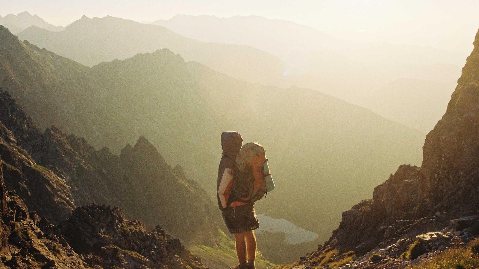 A hiker with a backpack walking a ridge line in low mountain cloud